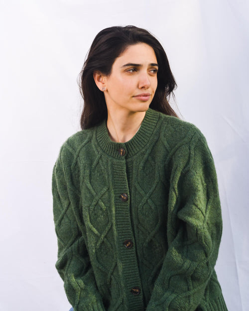 Woman wearing a green cable knit cardigan against a white background