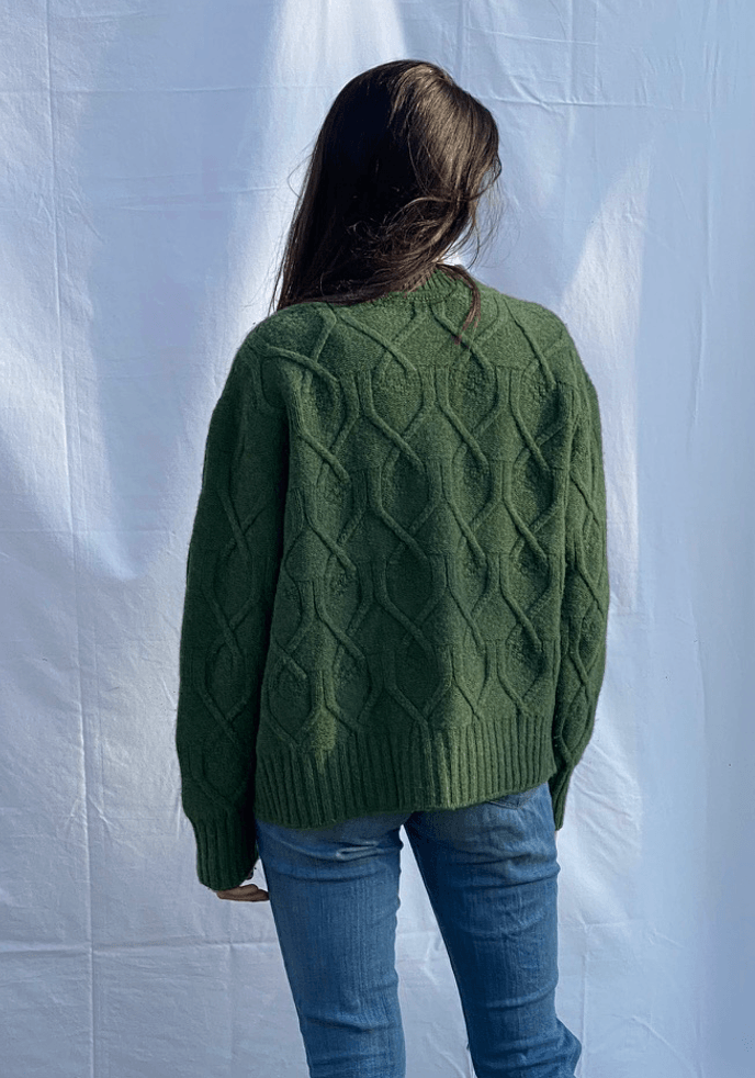 Woman wearing a green cable knit cardigan against a white background