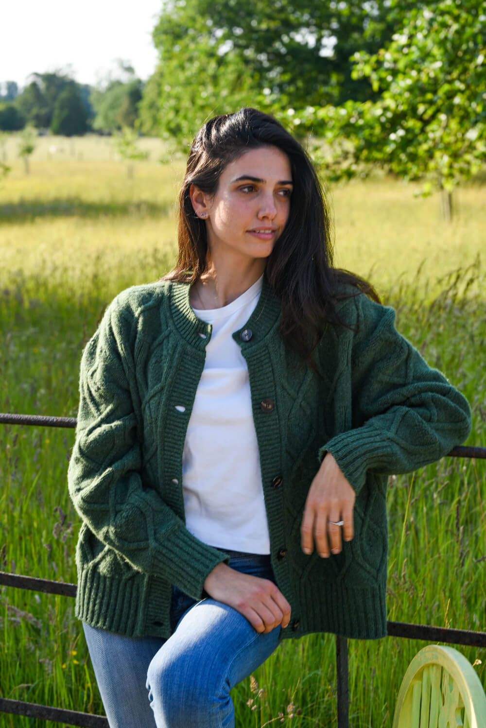 Woman wearing a green cardigan in a field with trees in the background