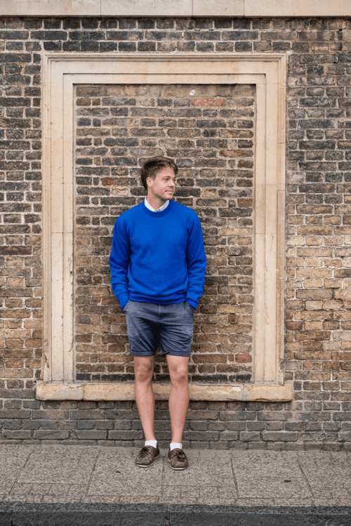 Man wearing a blue sweater and shorts standing in front of a brick wall 