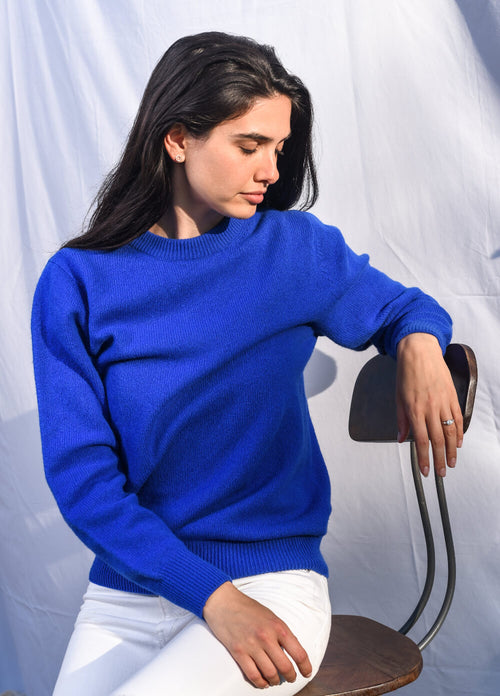 Woman wearing a blue sweater sitting on a chair against a white background