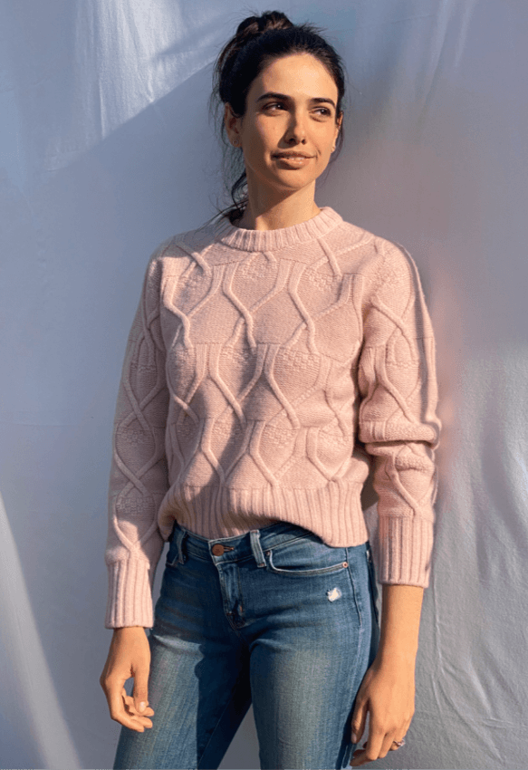 Woman wearing a pink cable knit sweater and blue jeans against a light background