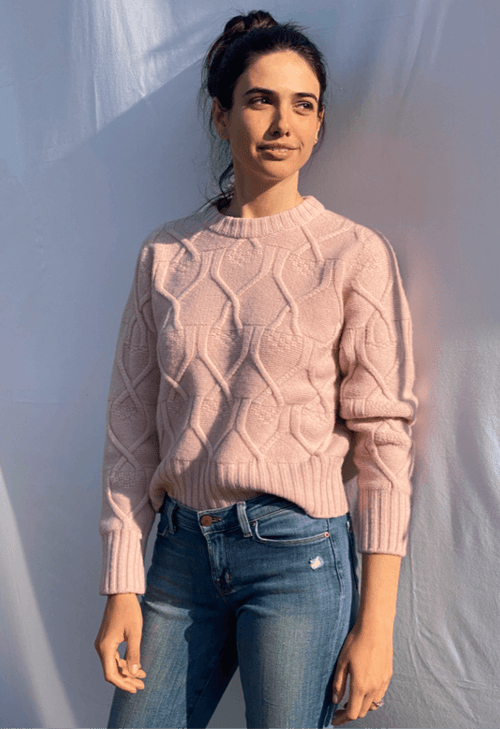 Woman wearing a pink cable knit sweater and blue jeans against a light background
