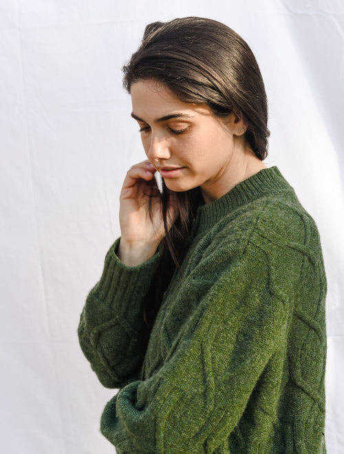 Woman wearing a green cable cardigan against a white background