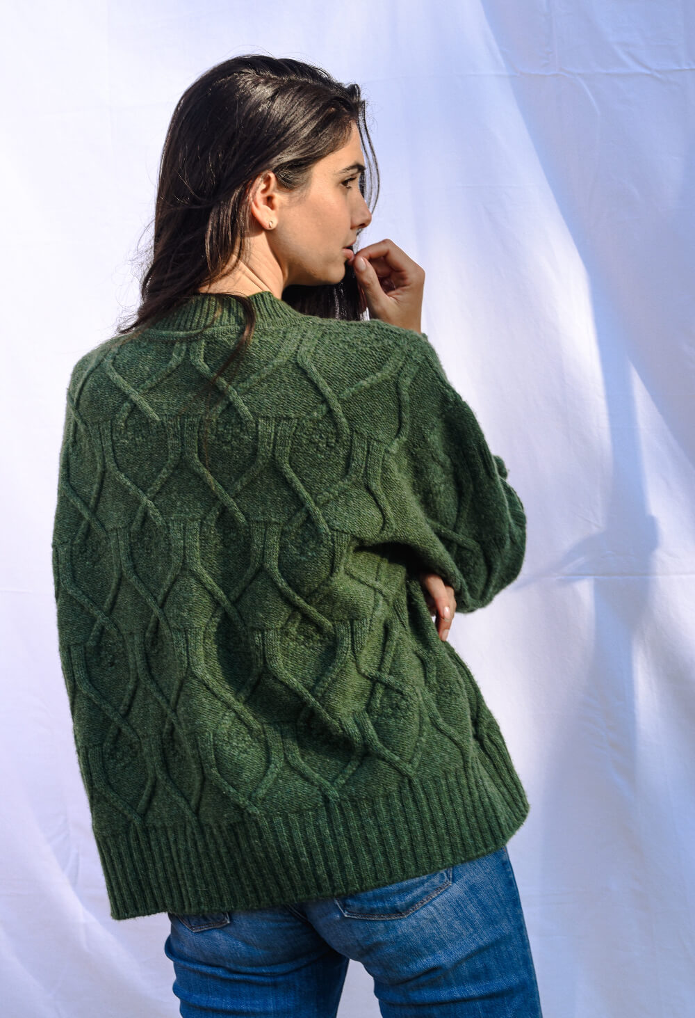 Person wearing a green cable knit cardigan against a white background