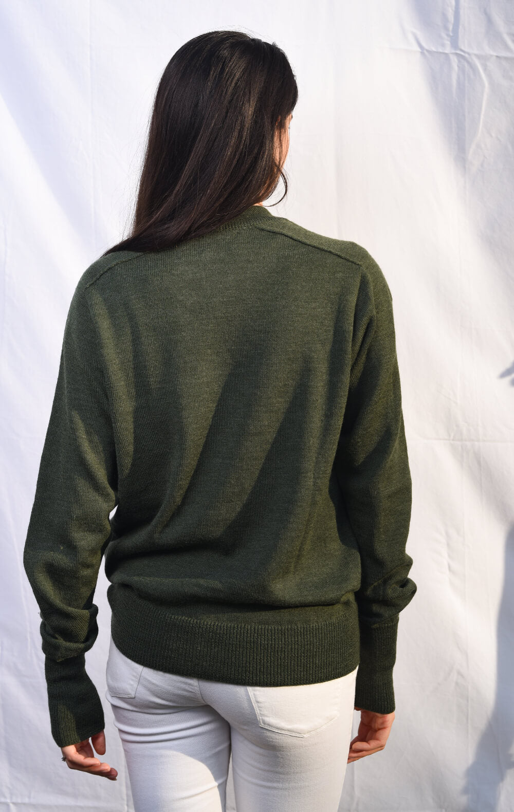 Person wearing a green sweater and white pants against a white background