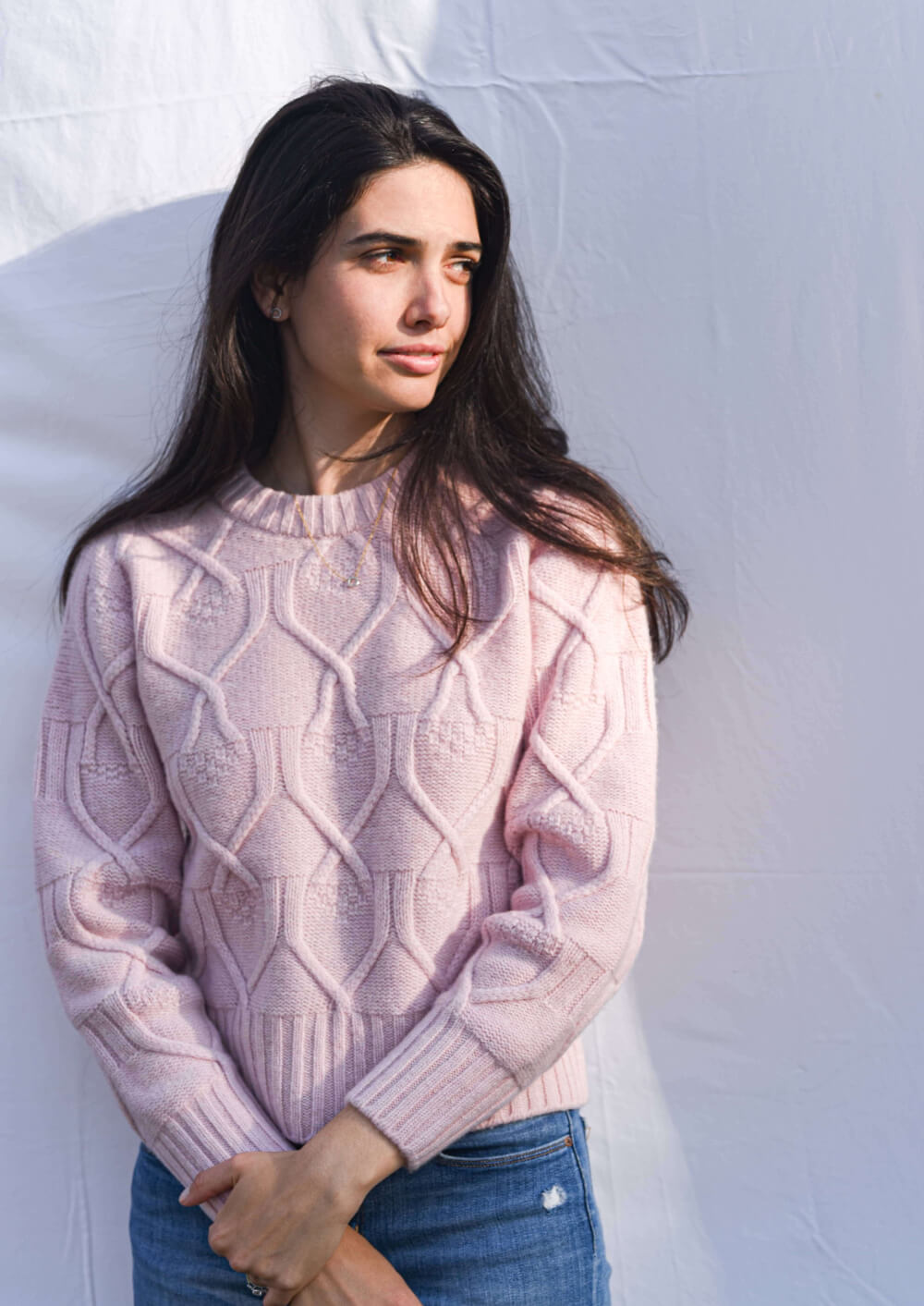 Woman wearing a pink cable knit sweater against a light gray background