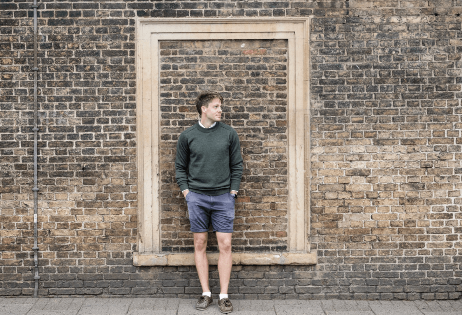 Man ewearing a merino wool crew neck jumper in green standing in front of a brick wall